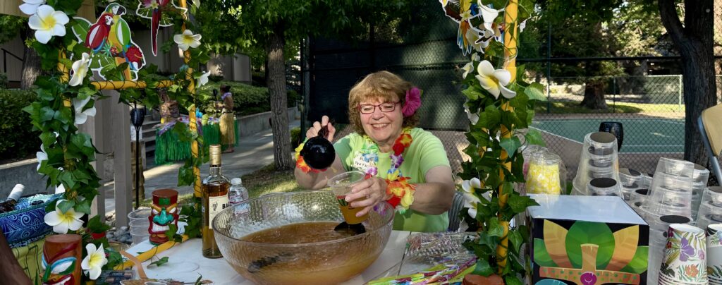 Committee member, Ellie Carpenter, cheerfully pouring punch at our 2025 Hawaiian party.